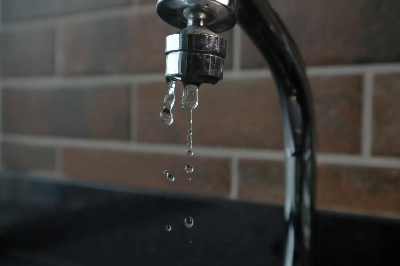 Faucet dripping water against a dark brick wall