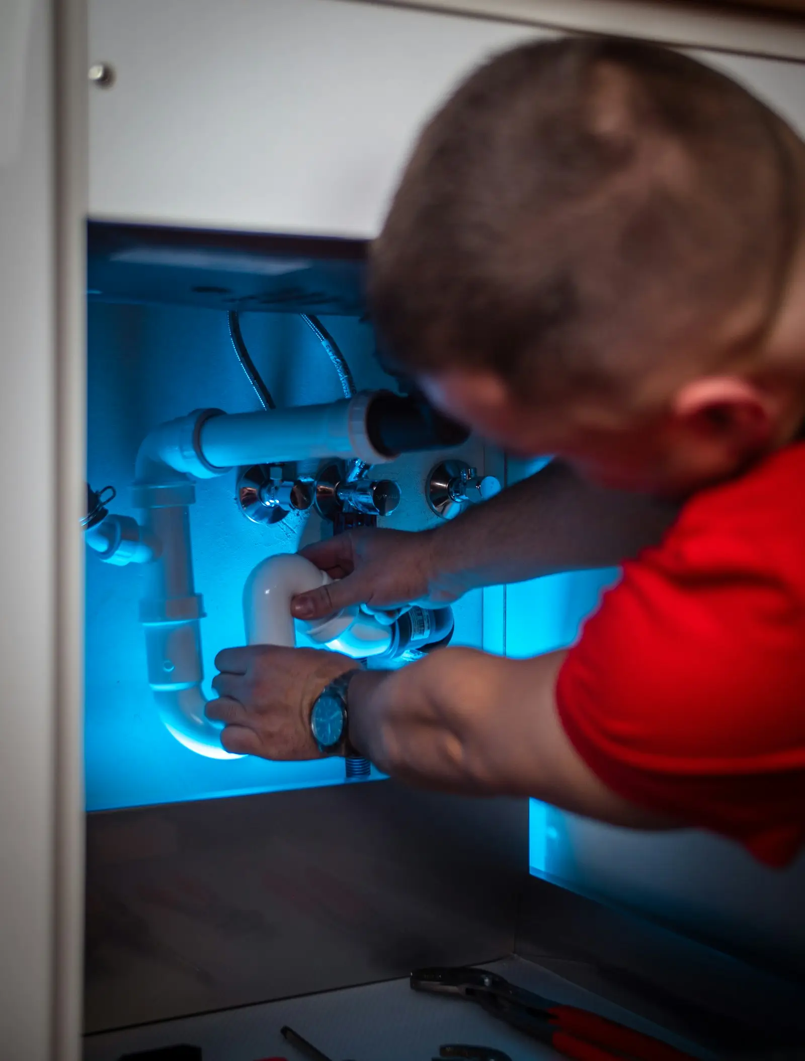 Plumber working on a plumbing manifold inside a utility cabinet
